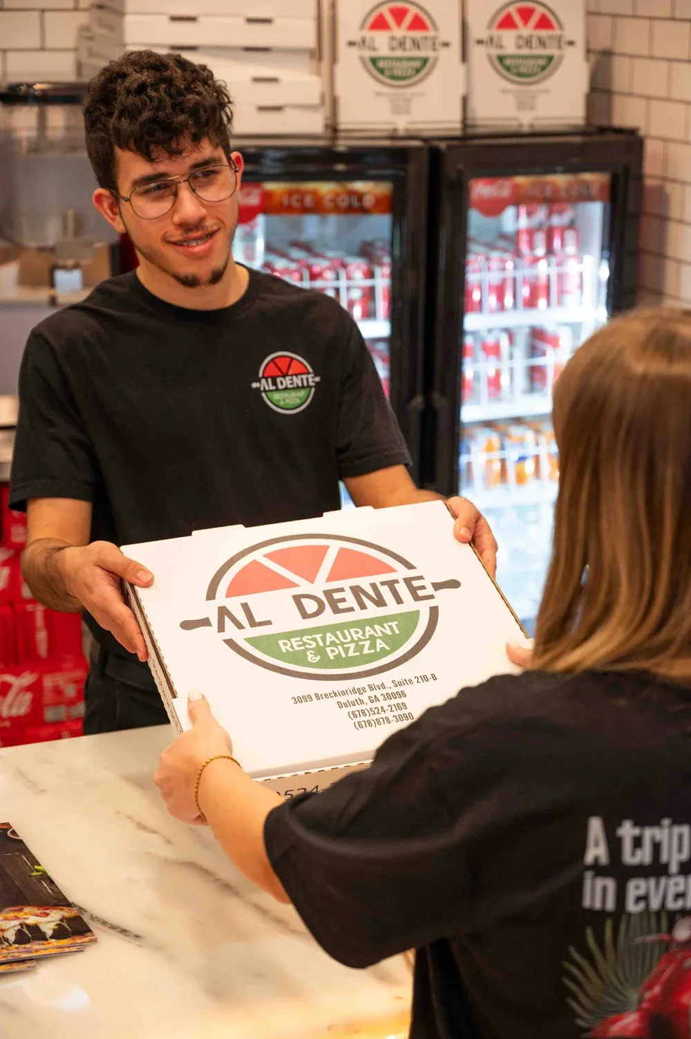 A team member handing an Al Dente pizza box across the counter to a guest