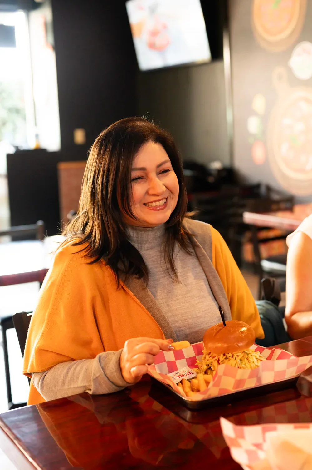 A guest laughing over a basket of burger and fries in the dining room