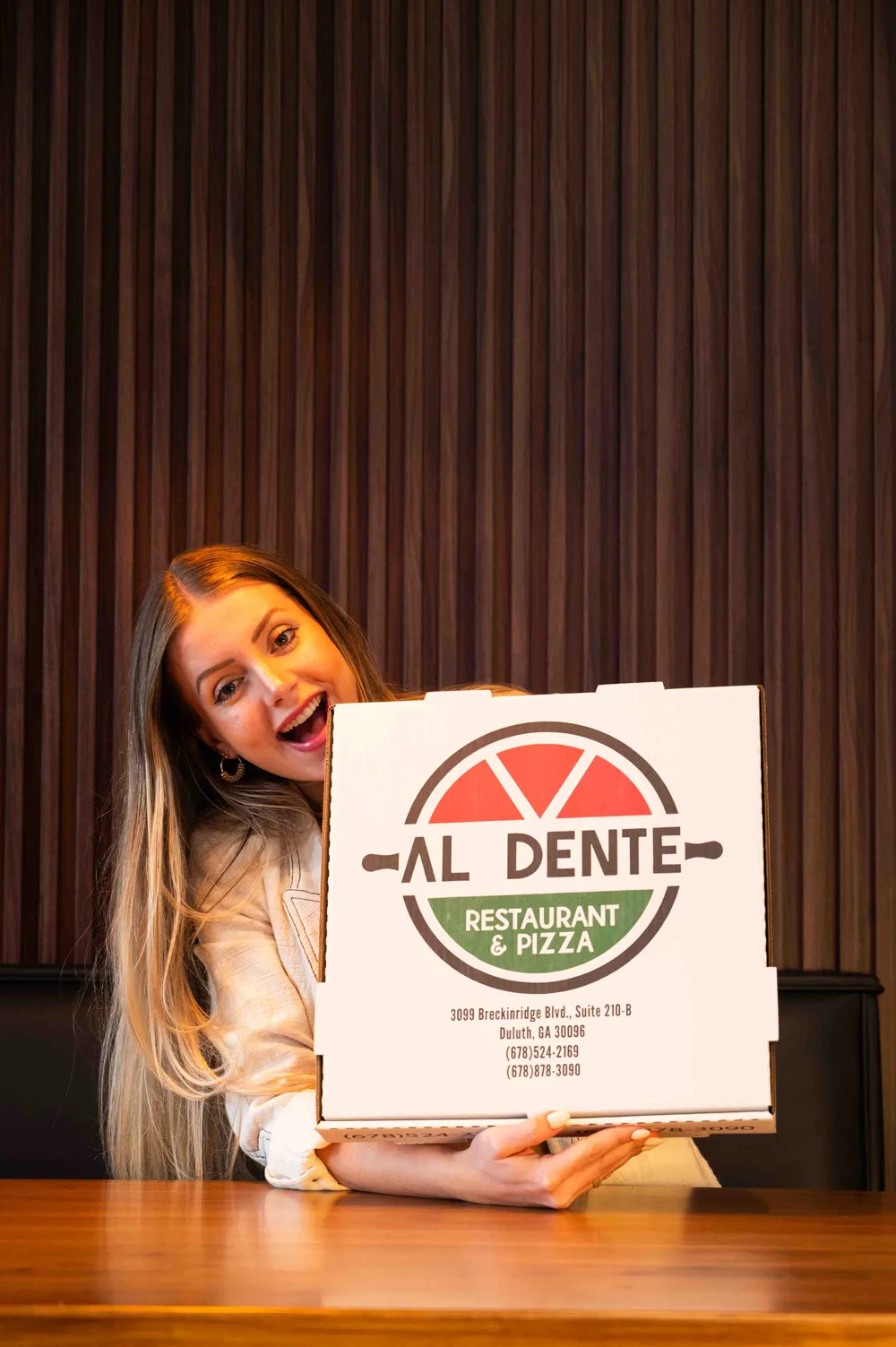 A guest grinning behind a large Al Dente pizza box at a table