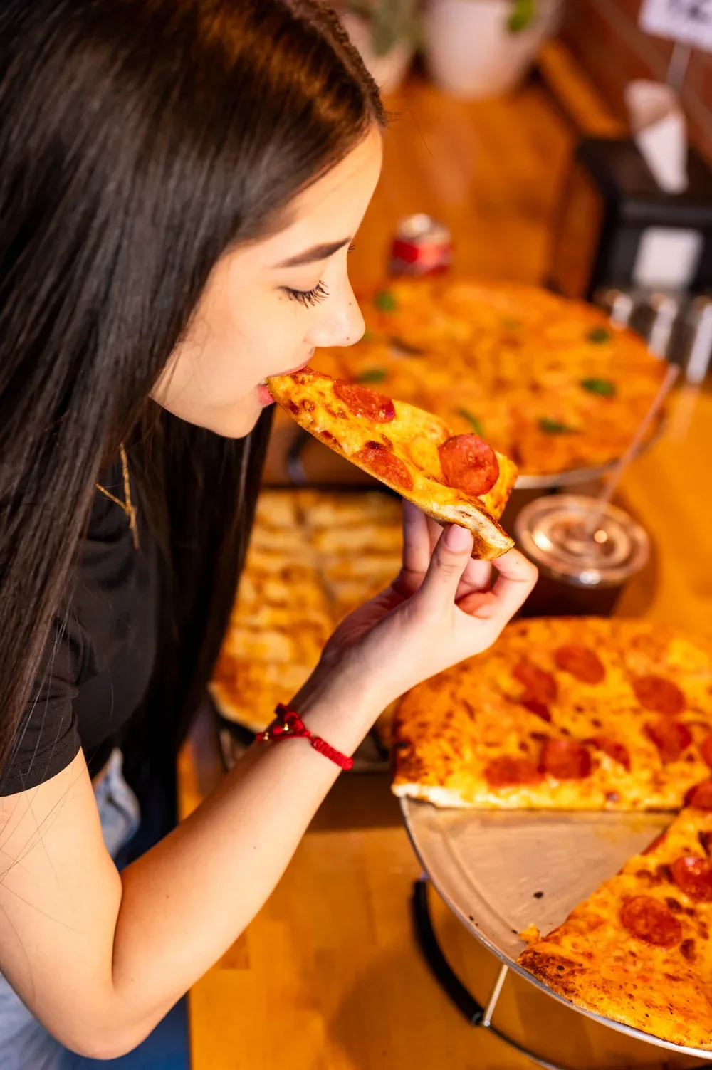 A guest taking a bite of a pepperoni slice over a table of pizzas