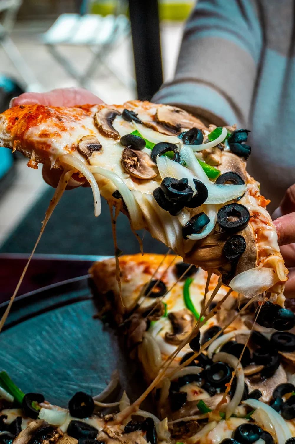 A slice of mushroom and olive pizza pulled away from the pie, cheese stretching